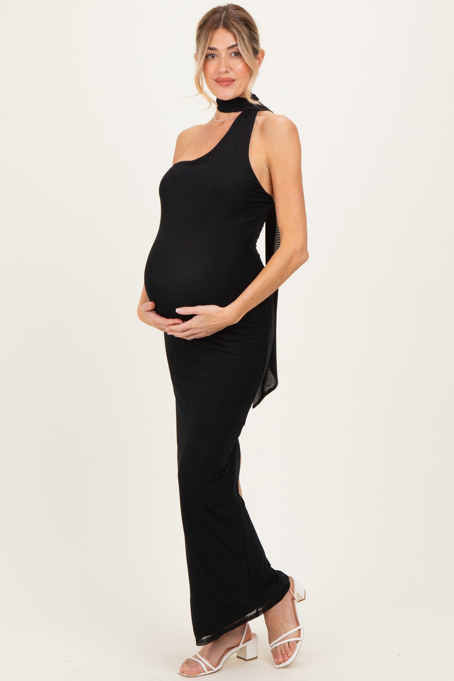 woman wearing a black one-shoulder maternity gown with a side slit and holding her baby bump