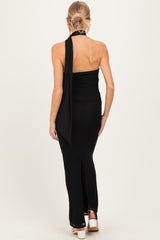 woman wearing a black maternity maxi dress with a halter neckline and a long back tie detail, showing a baby bump