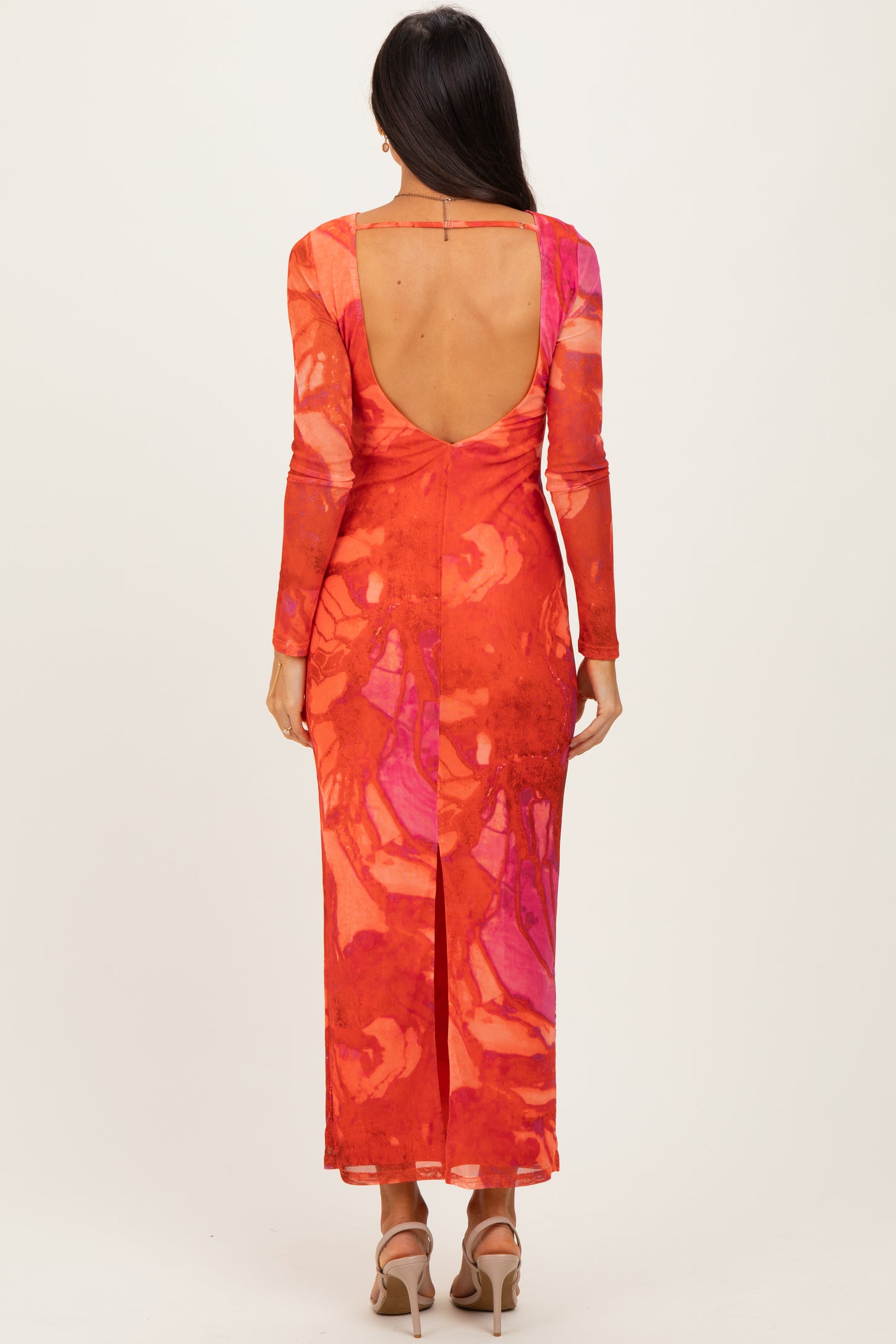 woman wearing a vibrant orange and pink long sleeve maxi dress with a deep back and side slit