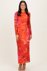 woman wearing a long sleeve red and pink abstract print maxi dress with a fitted silhouette and side slit