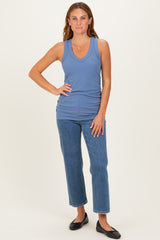 woman wearing a light blue ribbed tank top and high-waisted jeans, standing with hands on her hips