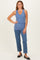 woman wearing a light blue ribbed tank top and high-waisted jeans, standing with hands on her hips