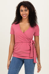woman wearing a pink wrap top with short sleeves and tie detail, paired with blue jeans