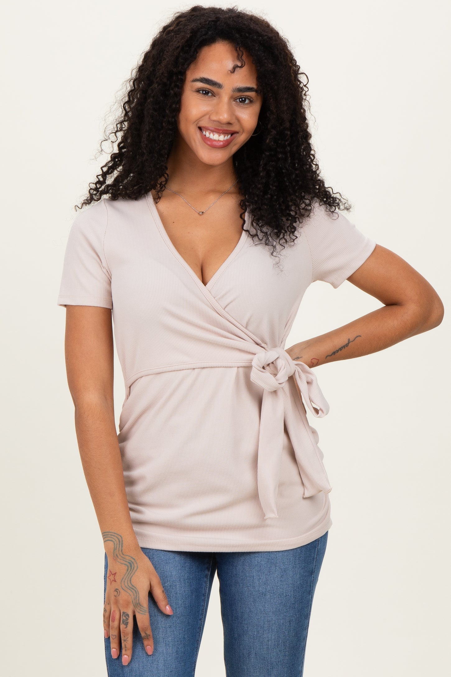 woman wearing a light pink wrap top with short sleeves and a tie detail at the waist, paired with blue jeans