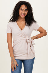 woman wearing a light pink wrap top with short sleeves and a tie detail at the waist, paired with blue jeans