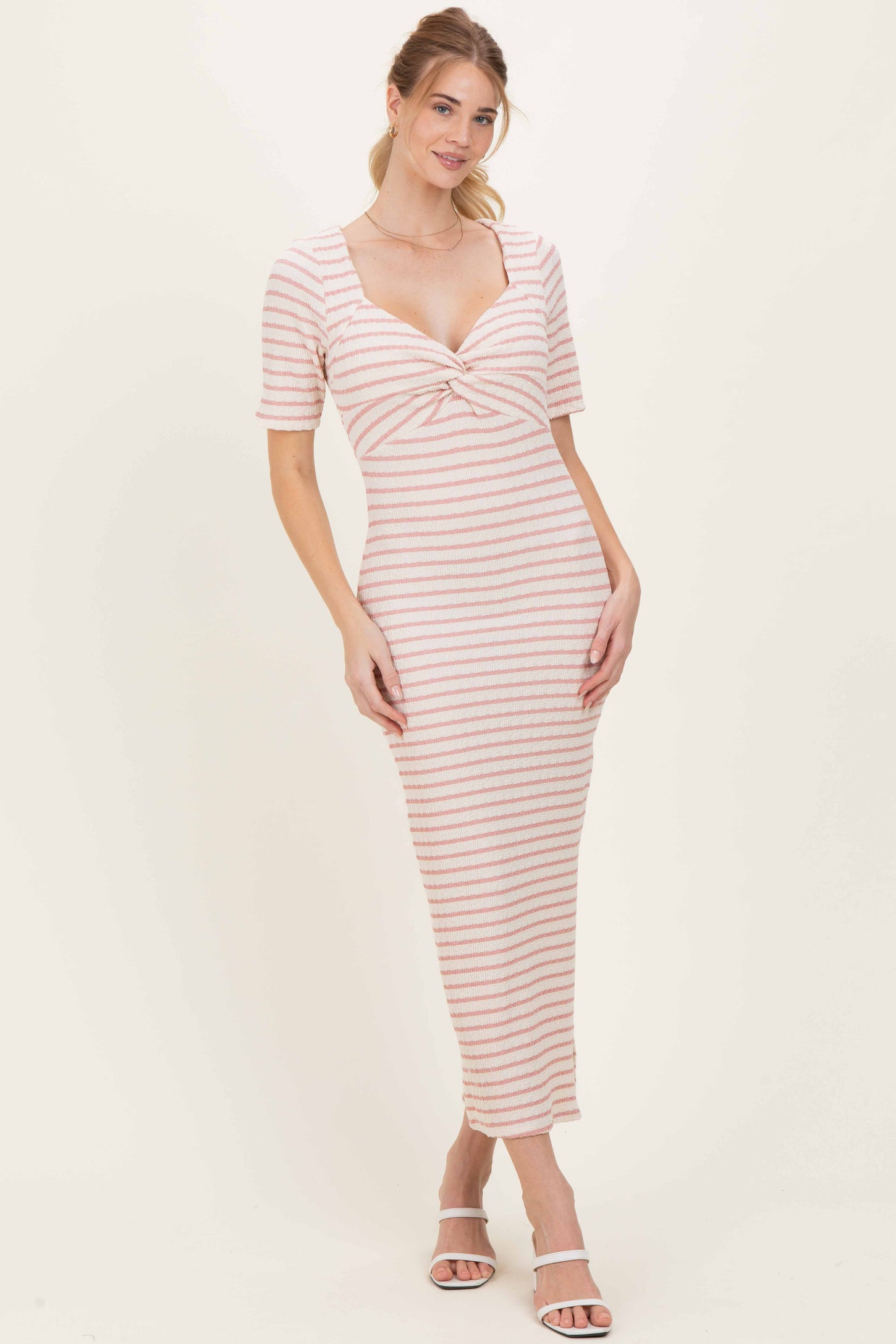 woman wearing a striped midi dress with a twisted front detail and short sleeves, standing in a neutral background