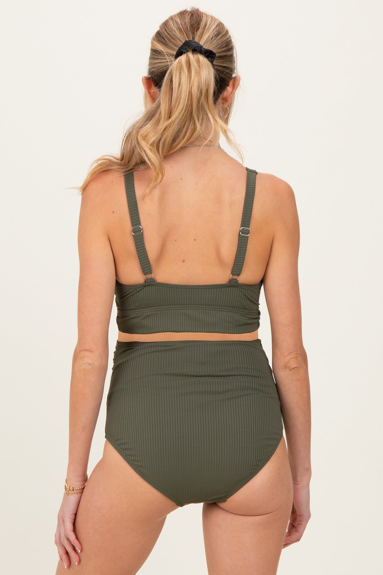 woman wearing a dark green ribbed maternity bikini top and high-waisted bottoms, showing a smooth back view