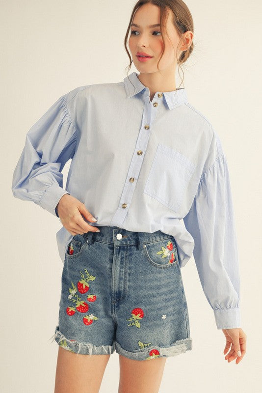 woman wearing a light blue button-up blouse with puff sleeves and denim shorts featuring strawberry embroidery