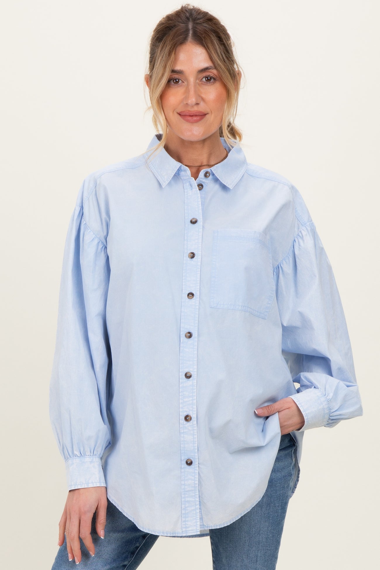 woman wearing a light blue maternity button-up shirt with puff sleeves and a chest pocket, smiling at the camera