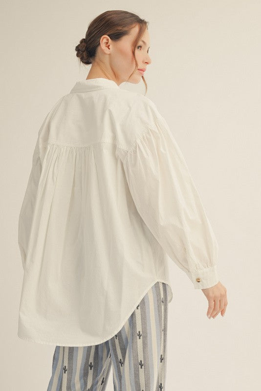 woman wearing a white oversized button-up shirt with a pleated back and long sleeves, styled with patterned pants