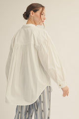 woman wearing a white oversized button-up shirt with a pleated back and long sleeves, styled with patterned pants