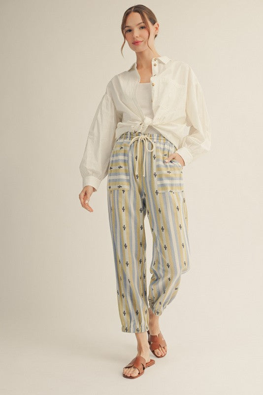 woman wearing a white button-up shirt and striped yellow and blue patterned pants with an elastic waistband and sandals
