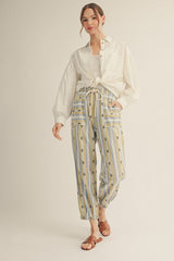 woman wearing a white button-up shirt and striped yellow and blue patterned pants with an elastic waistband and sandals