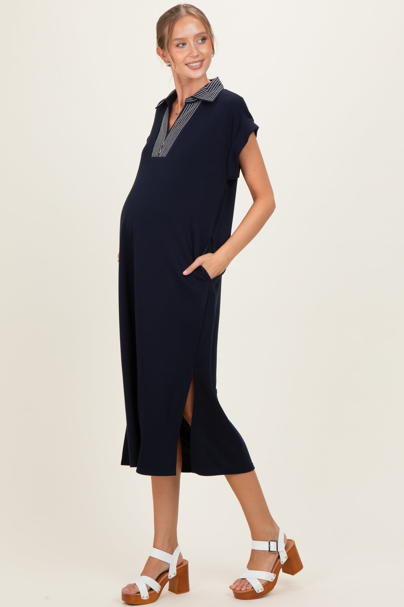 woman wearing a navy blue maternity dress with a collared neckline, side slits, and pockets, showing her baby bump