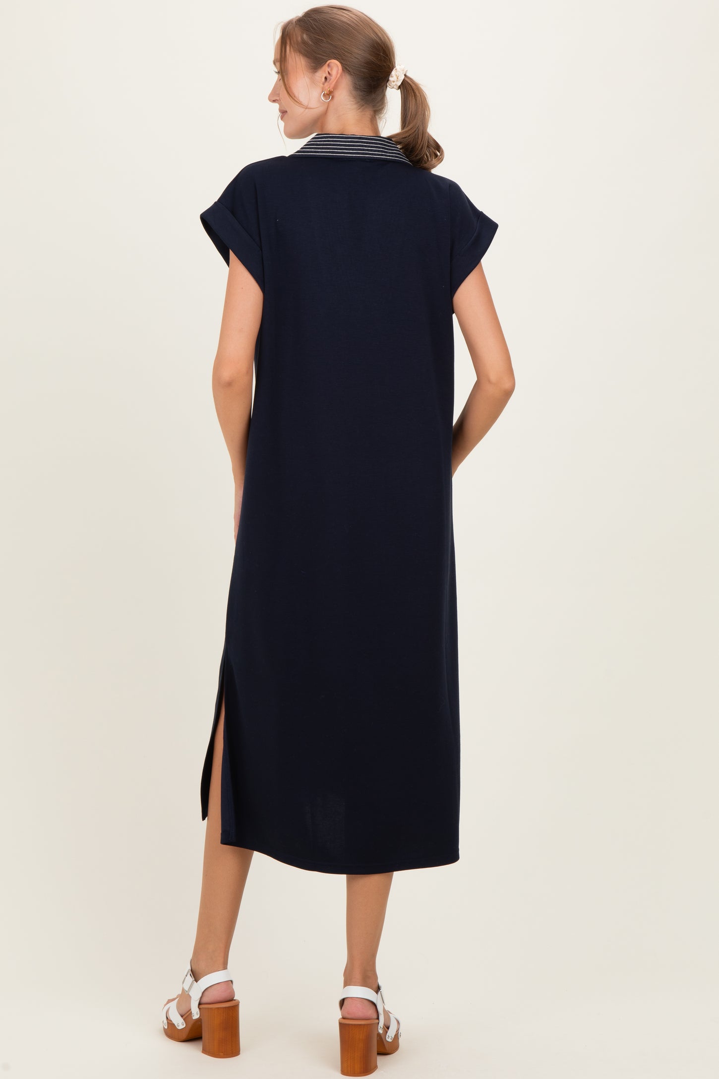woman wearing a navy blue maternity dress with a striped collar and side slits, showing her back
