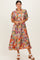 woman wearing a colorful floral print midi dress with short sleeves and a ruffled collar, standing and smiling