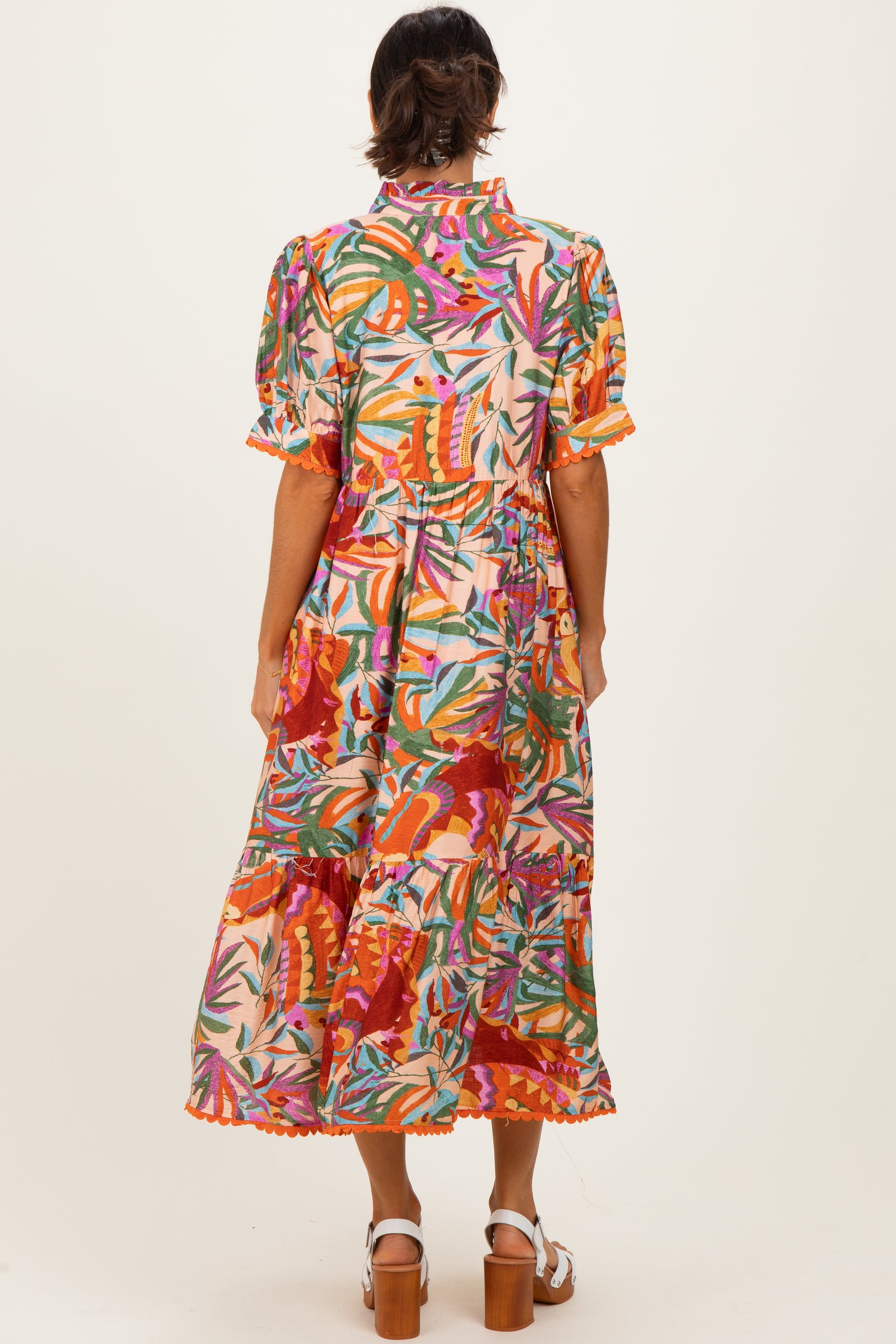 woman wearing a colorful floral print midi dress with puff sleeves and a ruffled hem, standing with her back to the camera