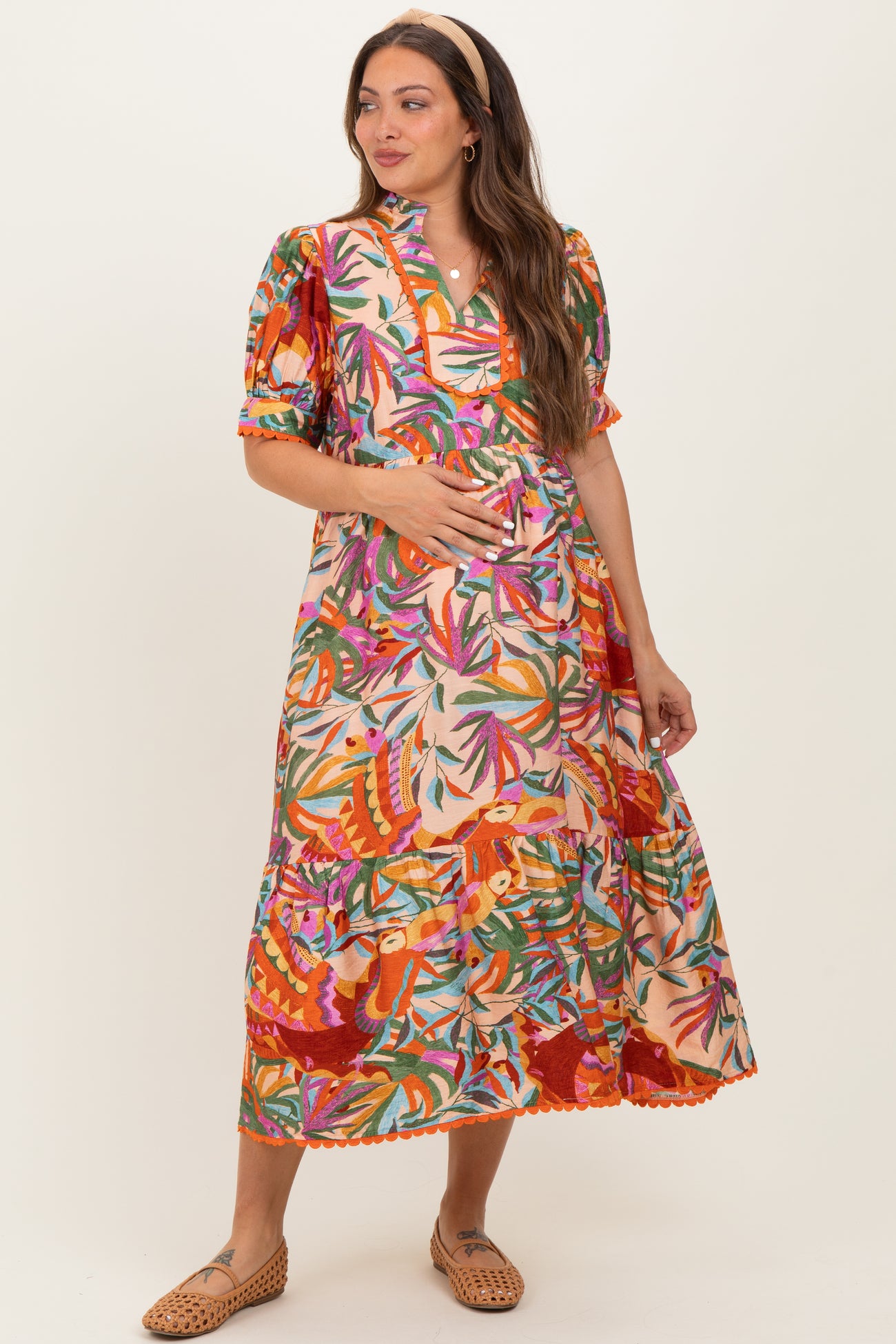 woman wearing a colorful floral print maternity dress with a tiered skirt and puff sleeves, holding her baby bump
