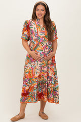 woman wearing a colorful floral maternity dress, smiling and cradling her baby bump