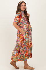 woman wearing a colorful floral print maternity dress with a tiered skirt and pockets, showcasing her baby bump