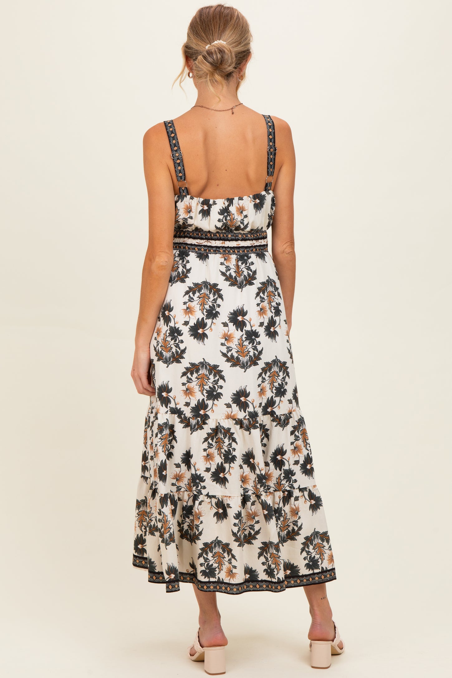 woman wearing a floral print white maternity dress with adjustable straps and a tiered skirt, showing a baby bump