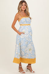 woman wearing a light blue floral maternity maxi dress with adjustable straps and pockets, showcasing her baby bump