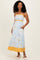 woman wearing a light blue floral maxi dress with yellow accents and pockets, standing against a plain background