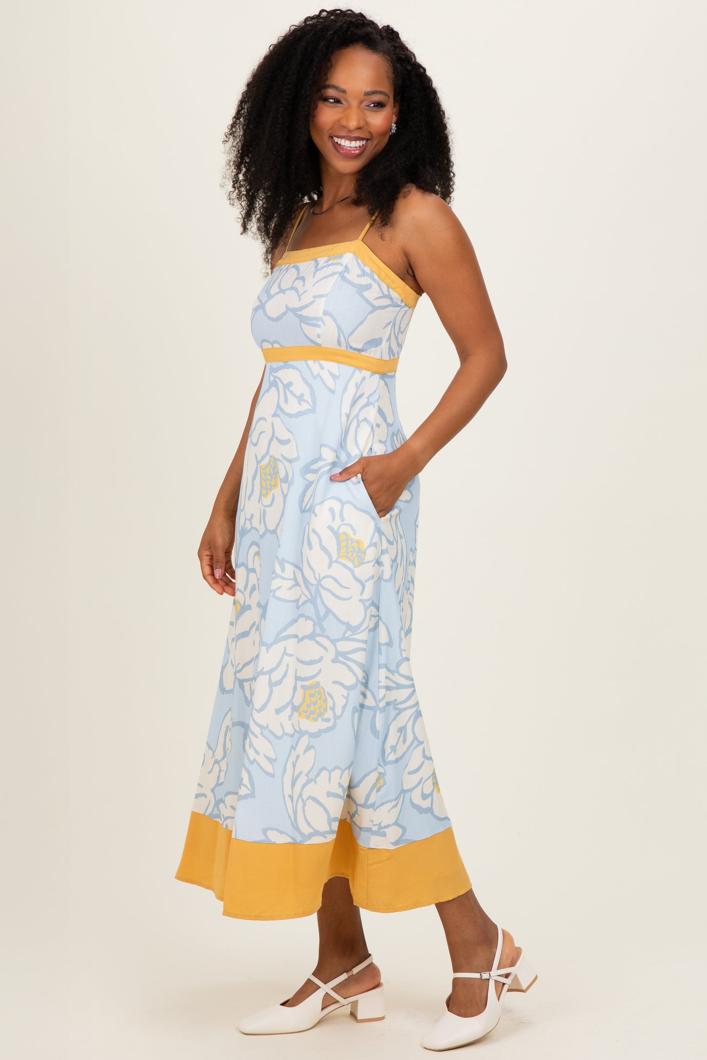 woman wearing a light blue floral maxi dress with yellow accents and pockets, styled with white sandals