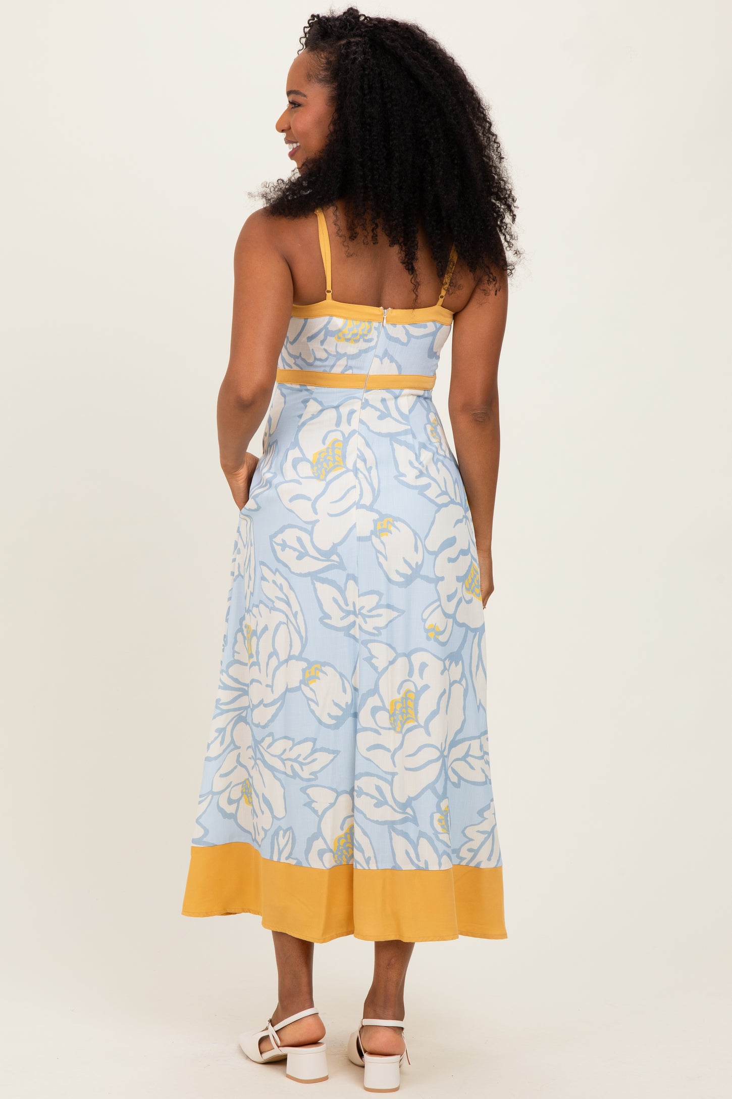 woman wearing a light blue floral midi dress with yellow trim, showing the back view and styled with curly hair