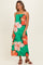 woman wearing a green floral maxi dress with orange and white flowers and thin straps