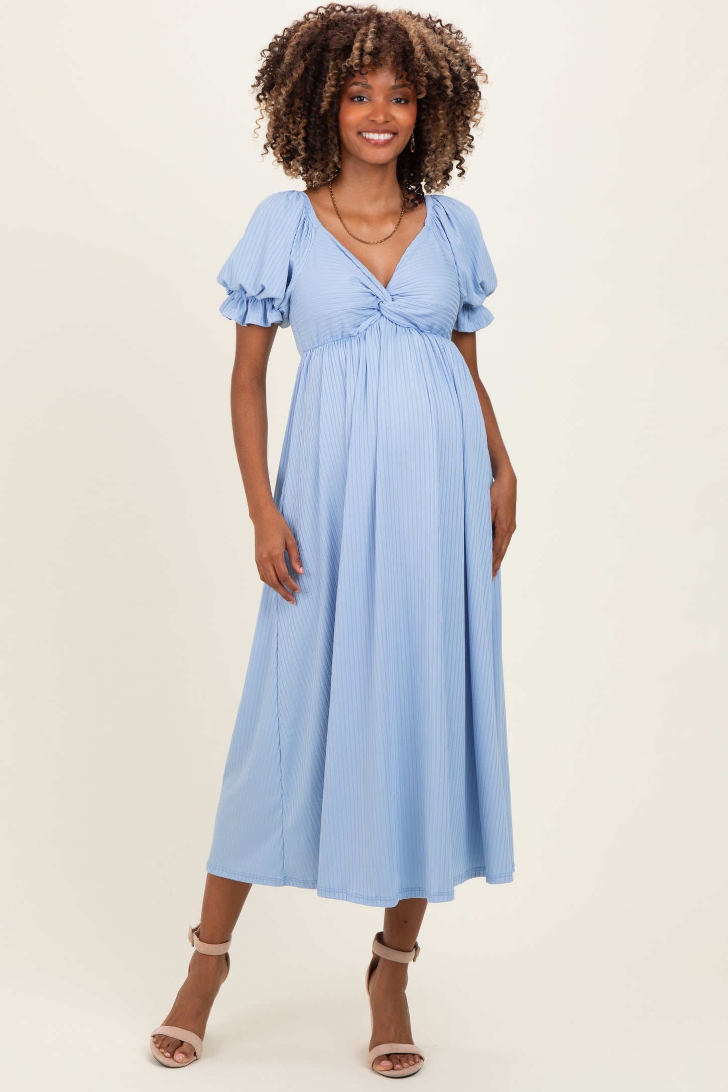 woman wearing a light blue striped maternity dress with short puff sleeves and a tie front, showing her baby bump