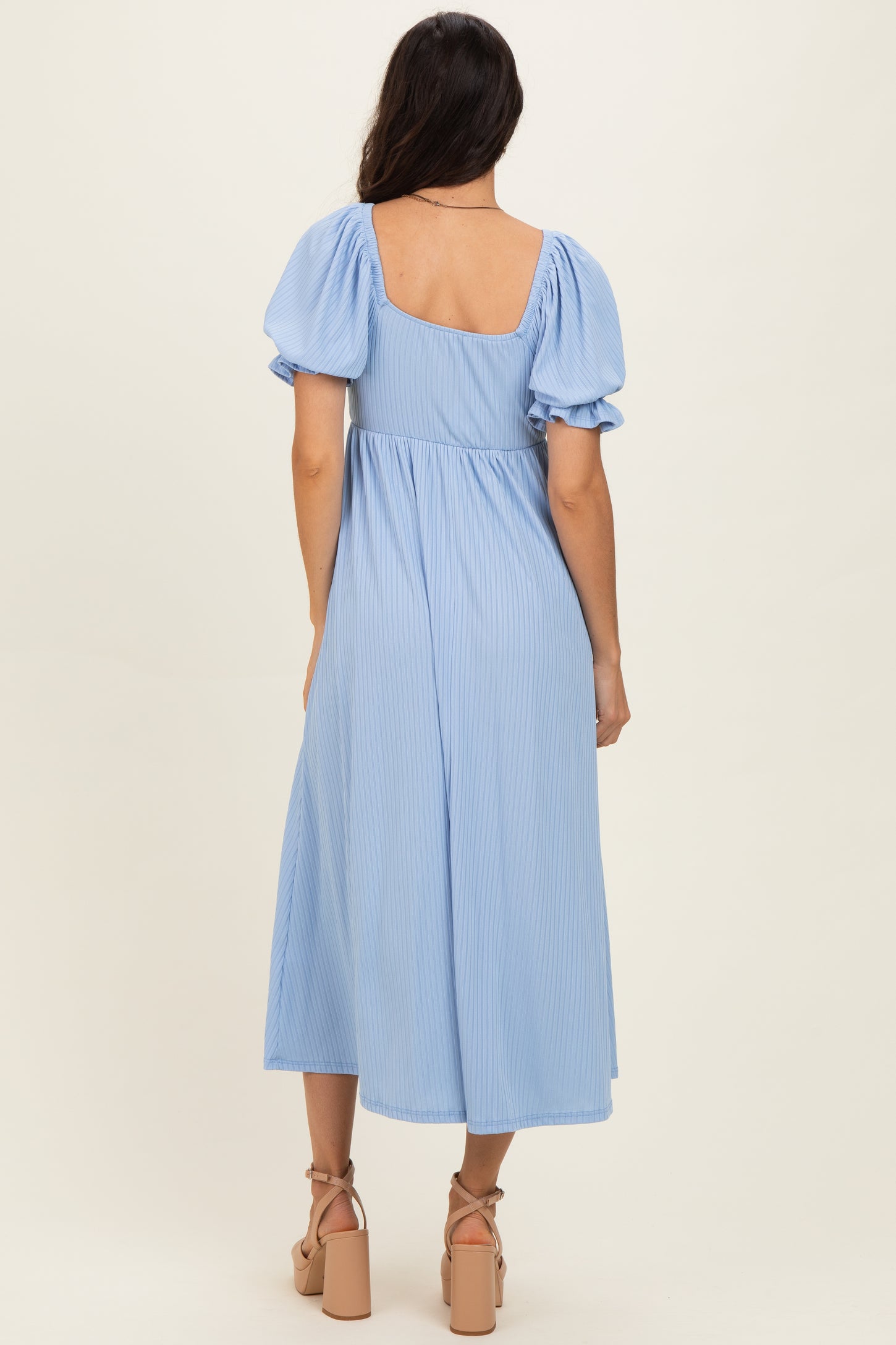 woman wearing a light blue midi dress with puff sleeves and a square back, standing in profile