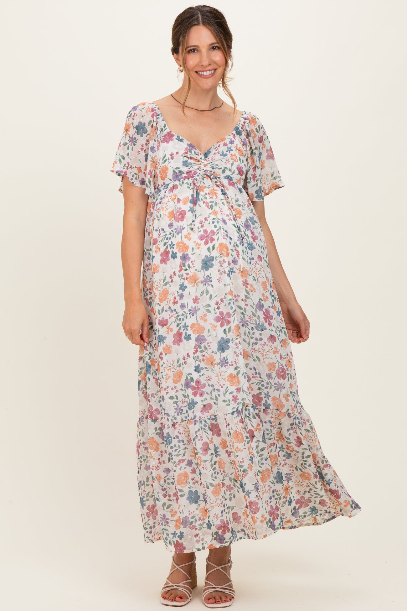 woman wearing a floral maternity maxi dress with a tie detail and short flutter sleeves, showcasing her baby bump