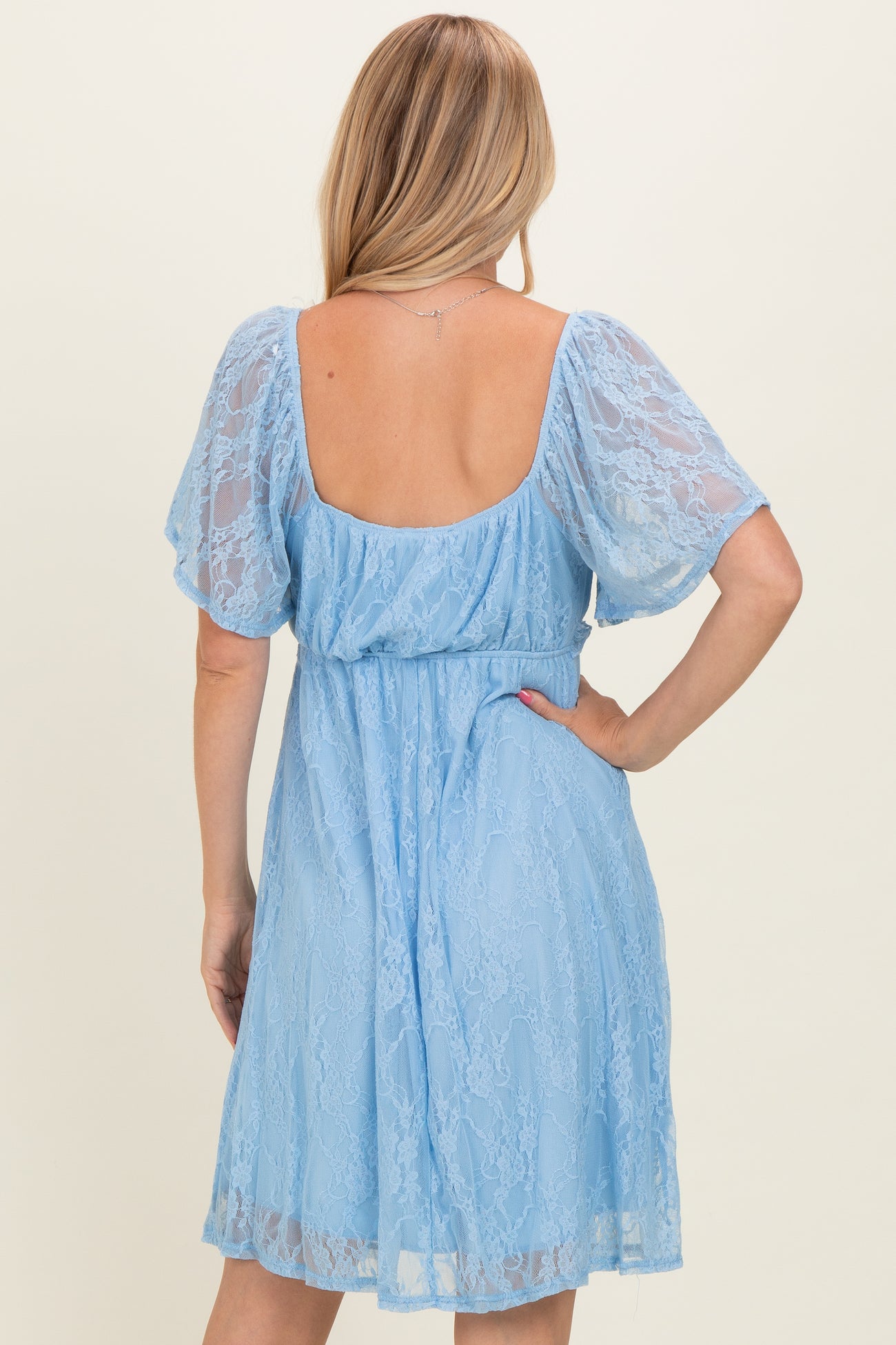 woman wearing a light blue lace dress with short puff sleeves and a cinched waist, showing a low back detail