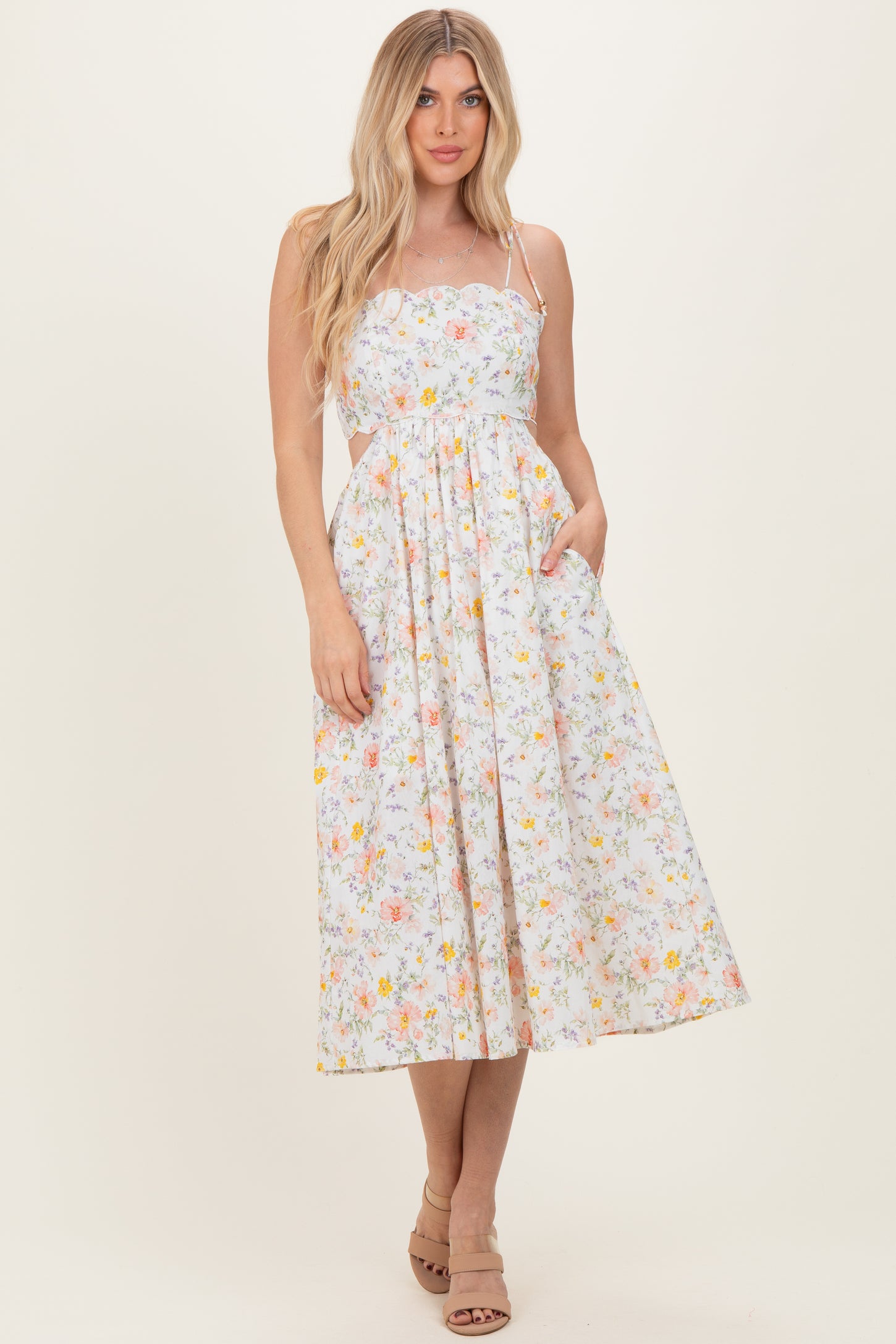 woman wearing a floral print midi dress with a fitted bodice and pockets, styled with strappy shoulders and a flowing skirt