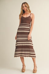woman wearing a brown and cream striped midi dress with spaghetti straps and a tiered hem, standing in a neutral background
