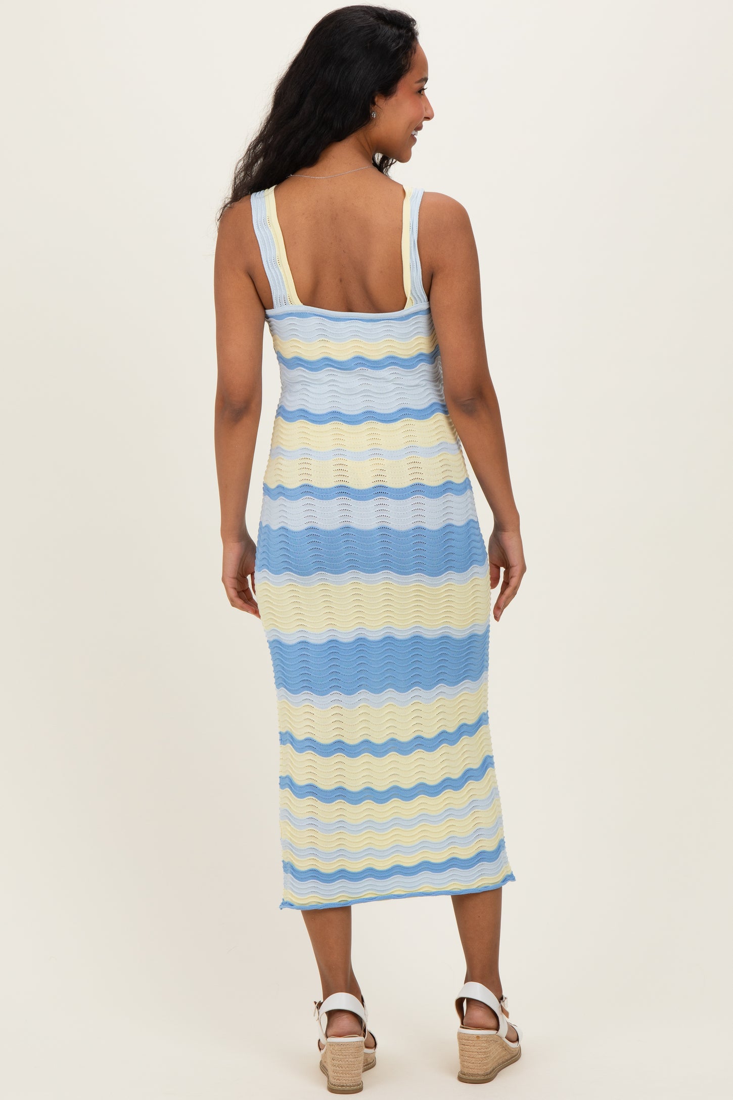 woman wearing a striped blue and yellow ribbed maternity dress, showing a comfortable fit and midi length from the back