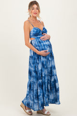 woman wearing a blue tie-dye maternity maxi dress with a cutout detail and holding her baby bump