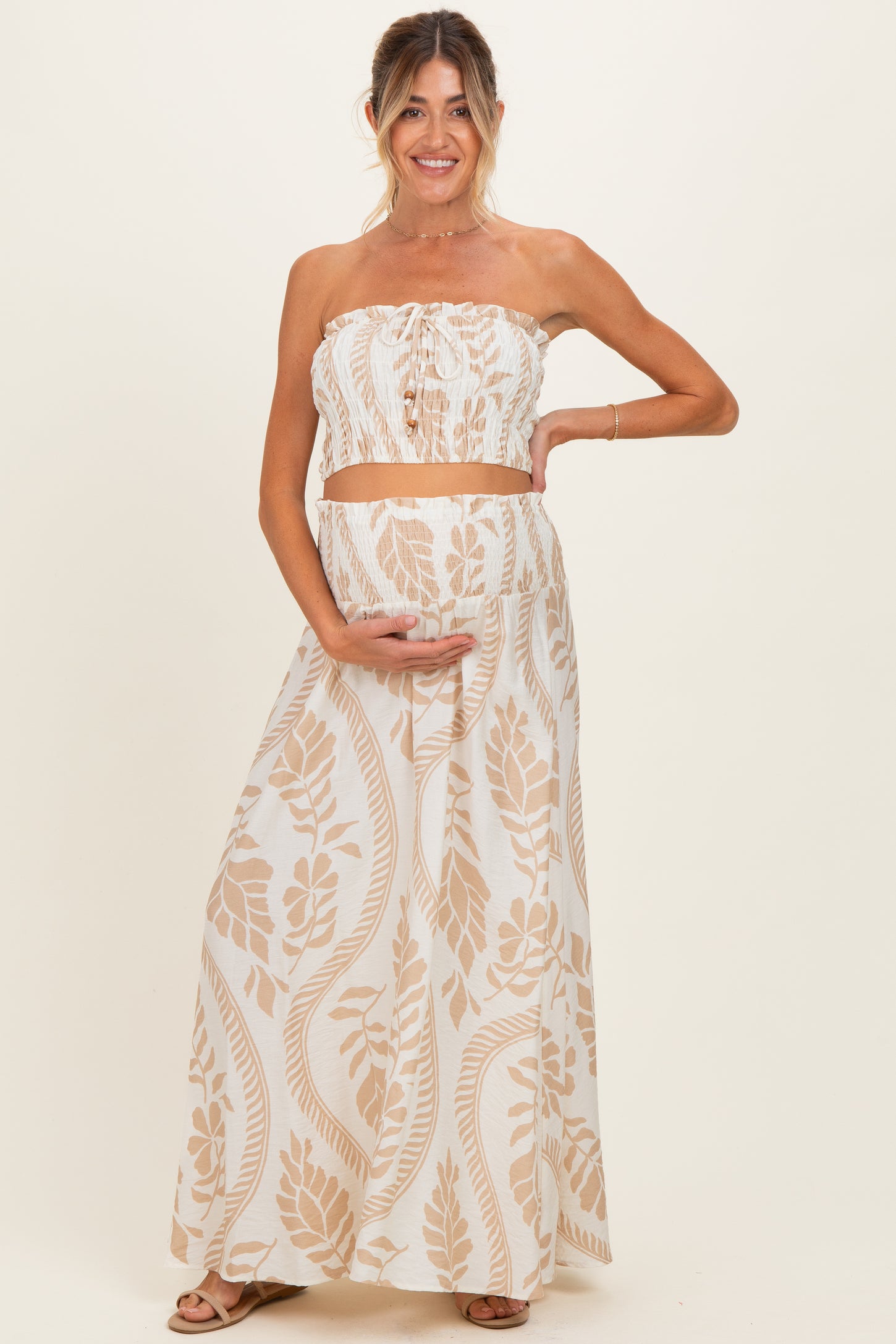 woman wearing a light brown floral print maternity two-piece set, showing her baby bump and smiling