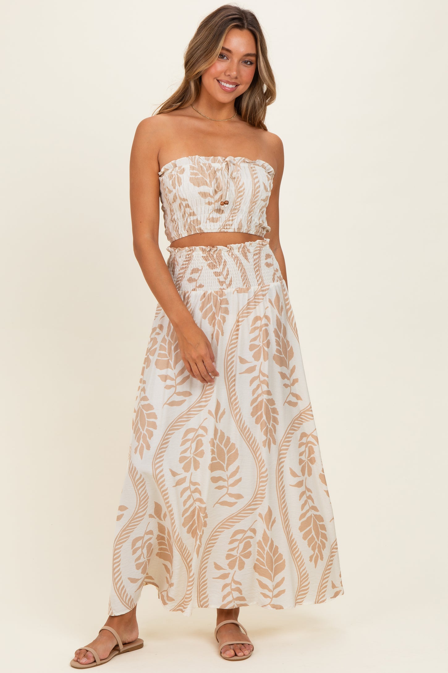 woman wearing a strapless crop top and matching maxi skirt with beige leaf patterns