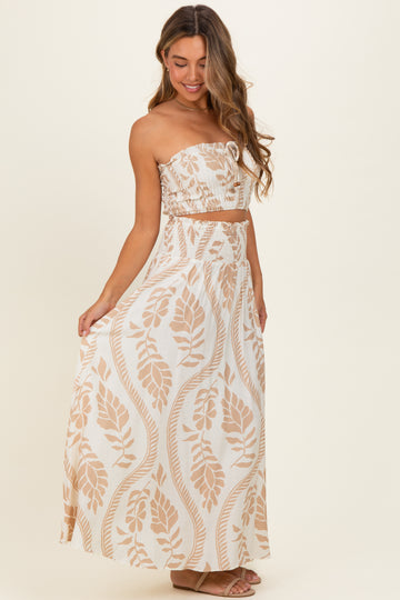 woman wearing a strapless beige and white maxi dress with a leaf pattern and a smocked waistband