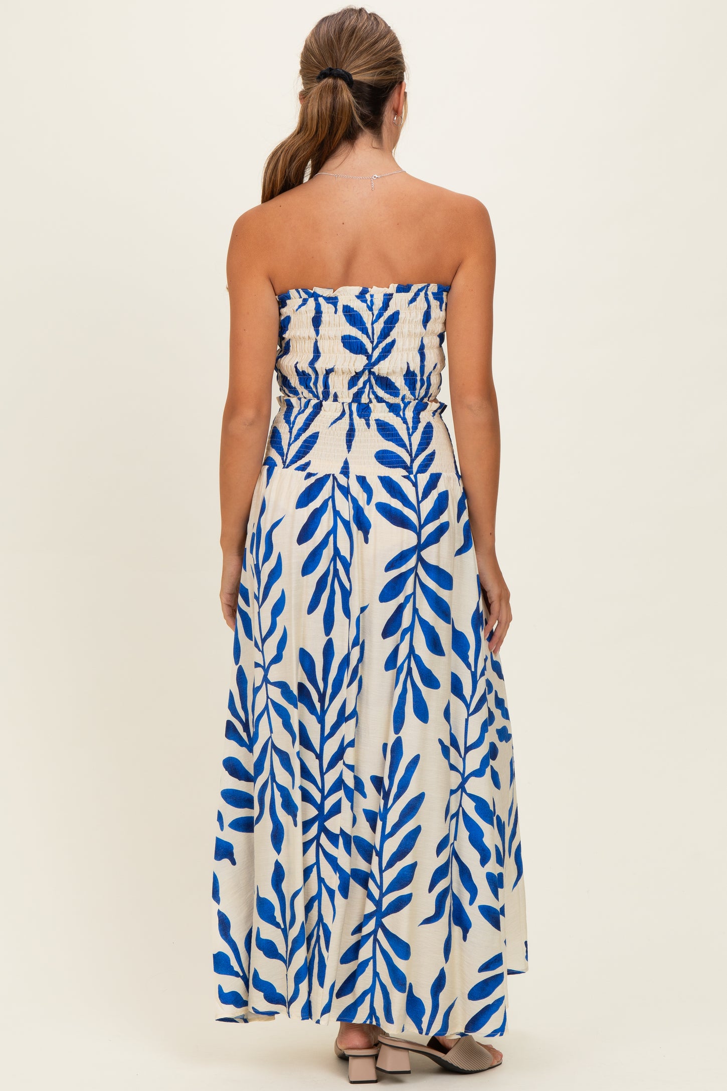 woman wearing a strapless maxi dress with a blue leaf print on a white background, showing the back view