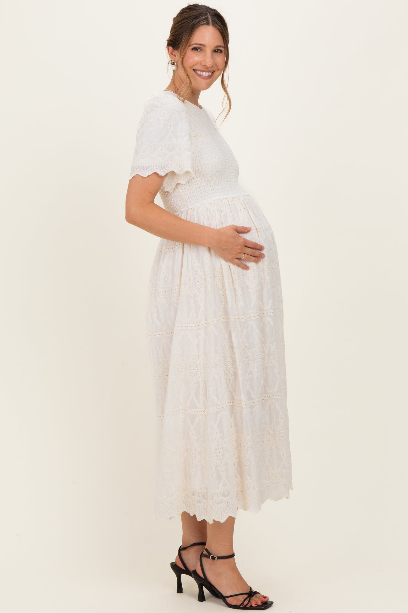 woman wearing a white lace maternity dress, smiling and holding her baby bump