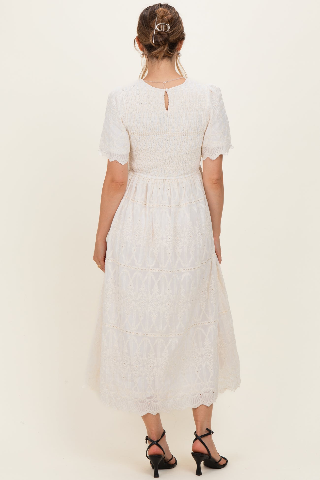 woman wearing a white maternity dress with short puff sleeves and a keyhole back, showing off a baby bump