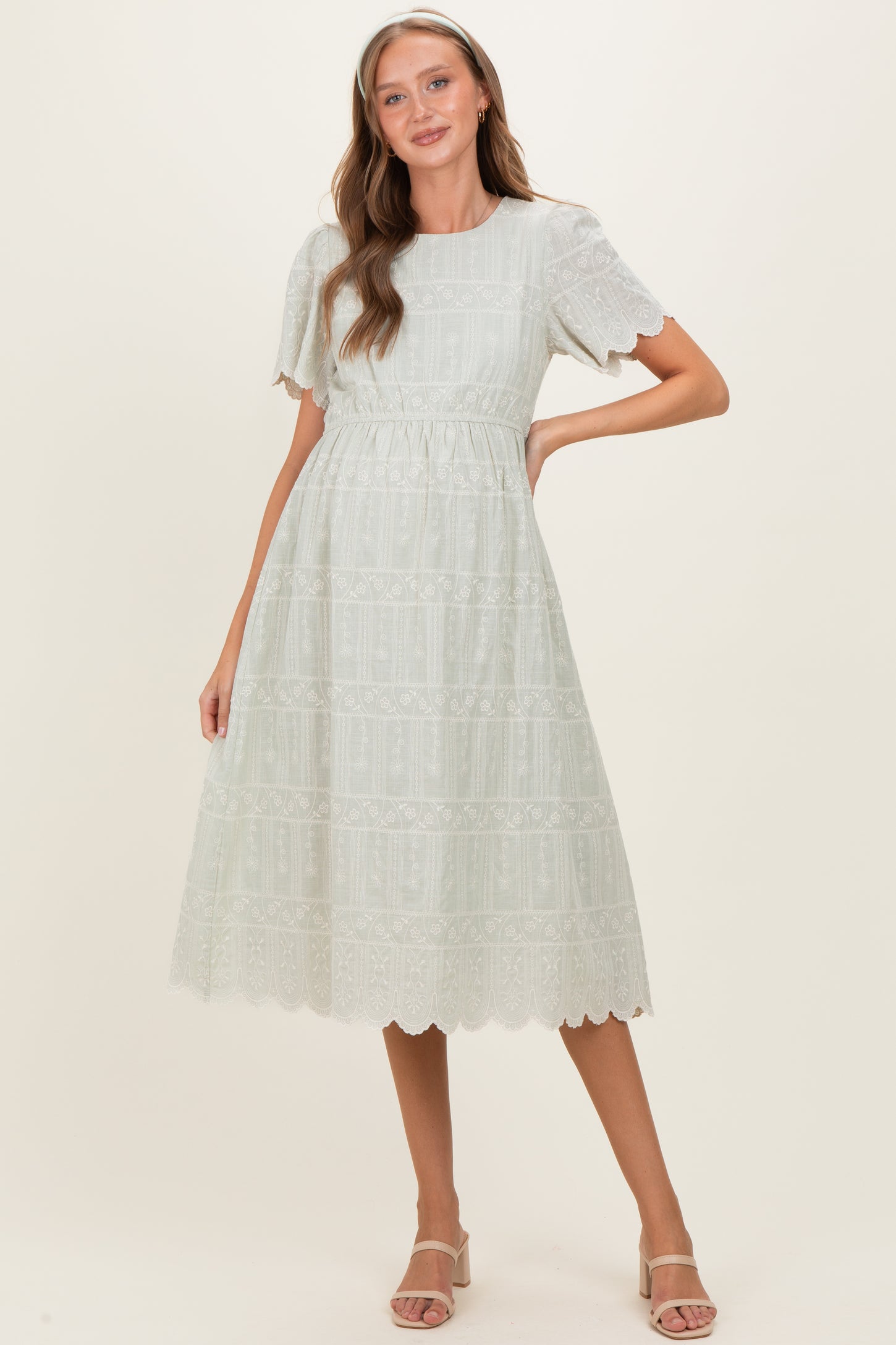 woman wearing a light green maternity dress with lace details and short flutter sleeves, styled elegantly with a flared skirt