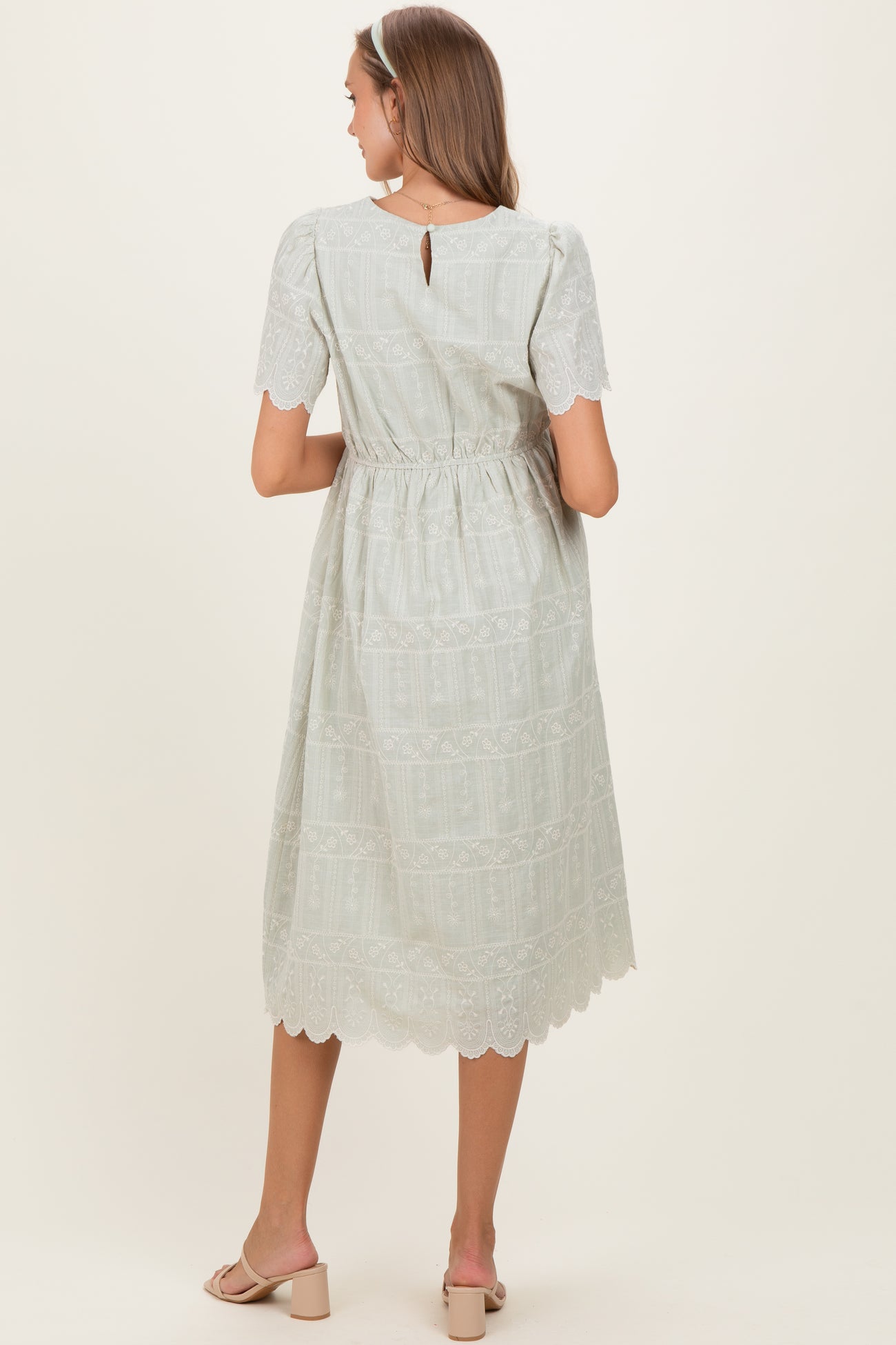 woman wearing a light green lace midi maternity dress with short sleeves and a cinched waist, showing a baby bump