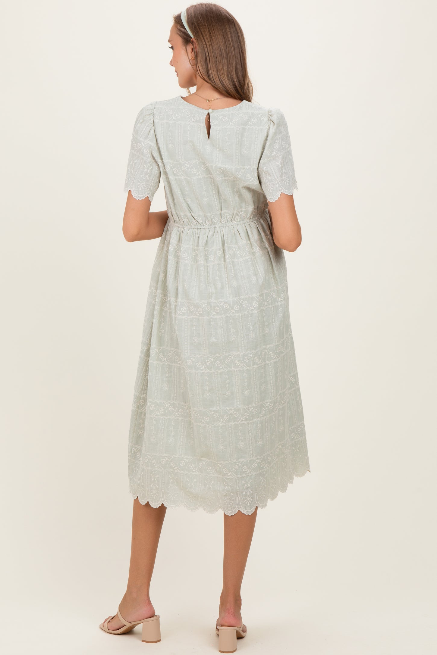 woman wearing a light green lace midi maternity dress with short sleeves and a cinched waist, showing a baby bump
