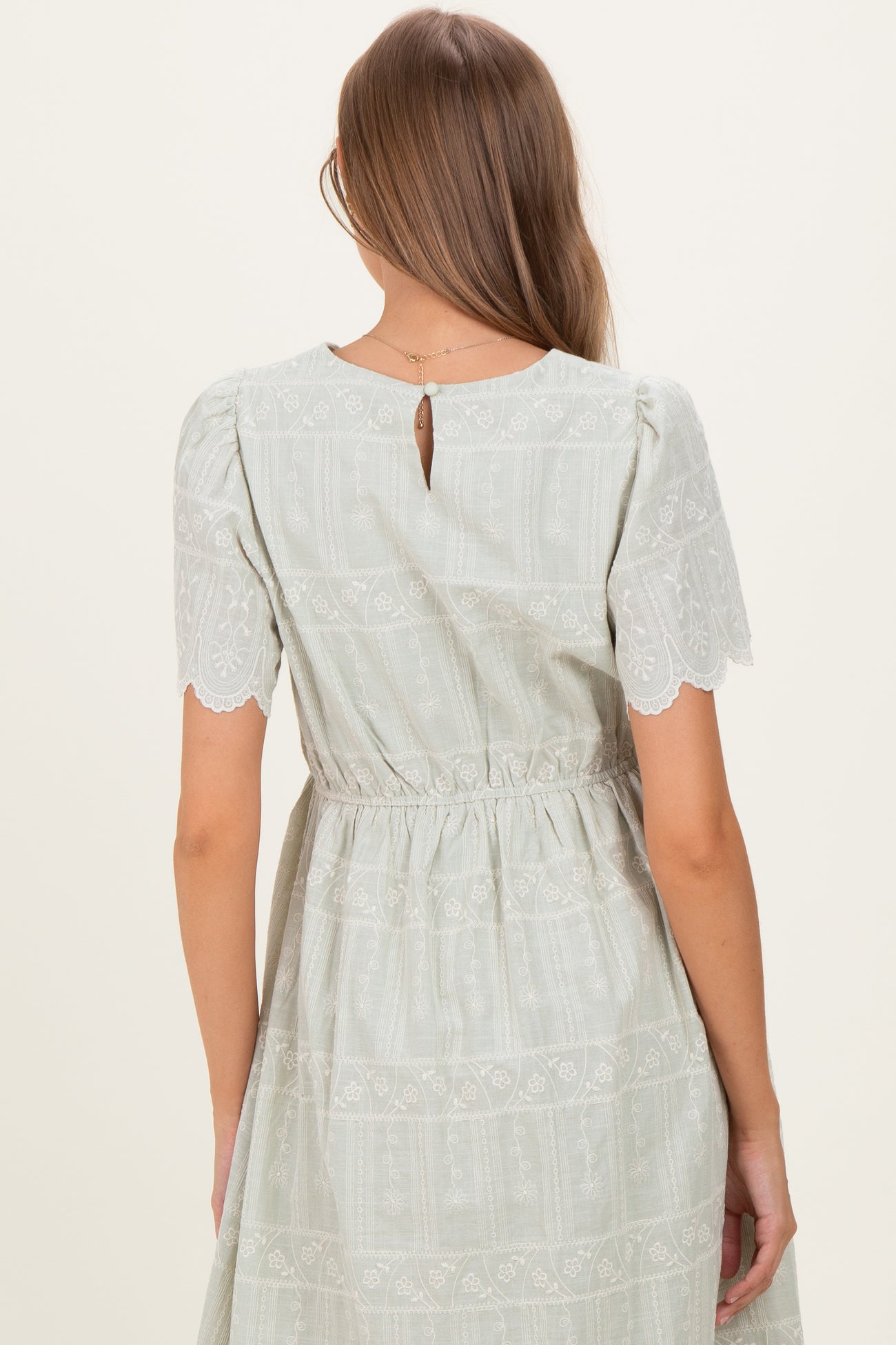 woman wearing a light green maternity dress with short lace sleeves and a keyhole back detail