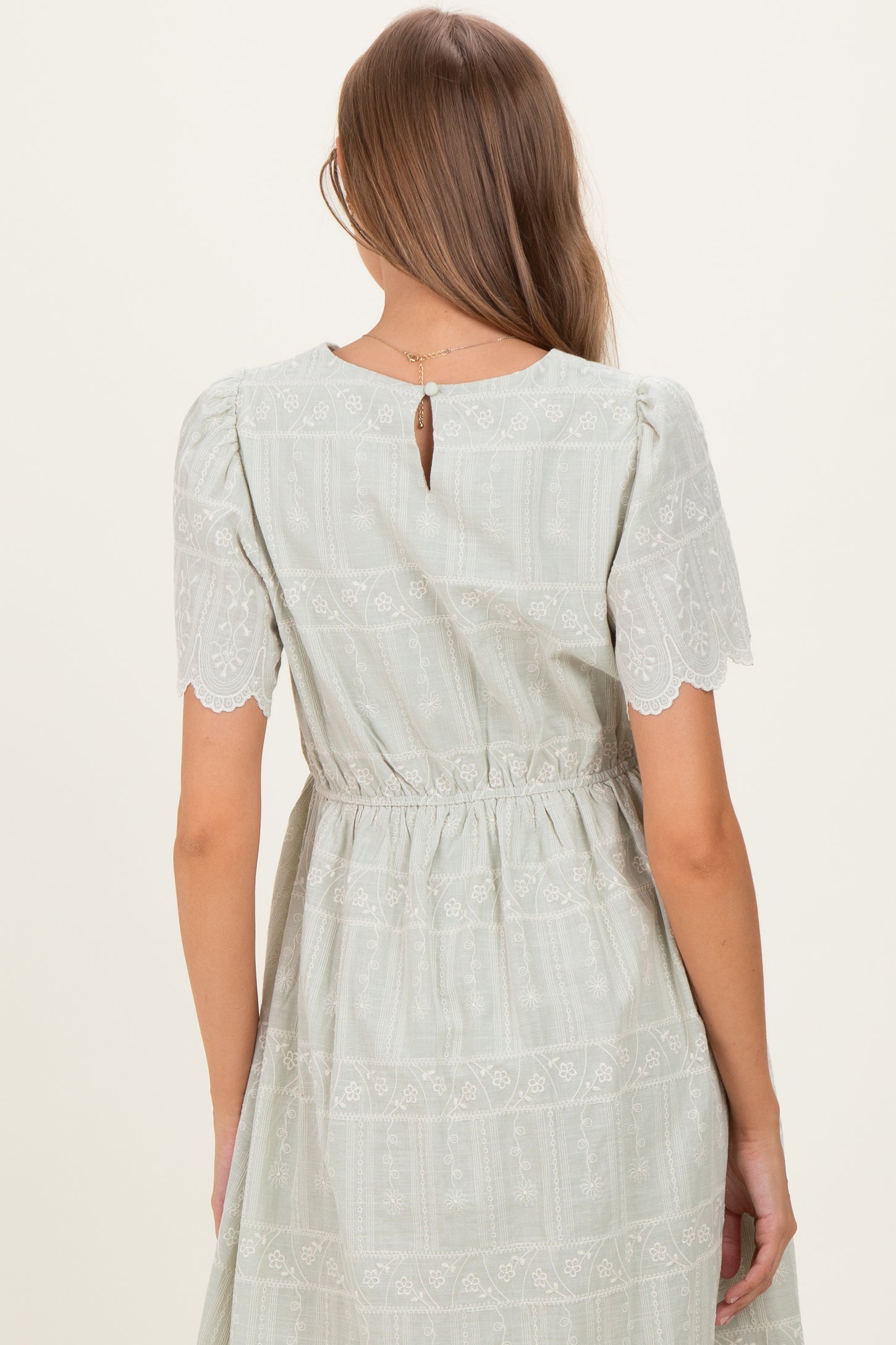 woman wearing a light green maternity dress with short lace sleeves and a keyhole back detail