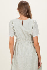 woman wearing a light green maternity dress with short lace sleeves and a keyhole back detail